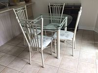 Full view of circular glass top metal kitchen table with 4 matching metal chairs with fabric seats.