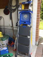 Three ladders grouped together in garage with visible marks and paint shelf on Costco ladder.