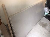 Top surface of a light gray resin folding table showing rectangular shape, slight marks, placed against a wall on garage floor.