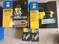 Original packaging for Power Fist 7 Amp Electric Plunge Router and 2-in-1 Air Stapler with two boxes of staples on floor.