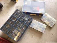 Image showing four plastic organizers on floor: one large cabinet with many small drawers, one large parts organizer with clear lid, and two smaller parts containers.