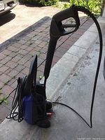 Side view showing blue and black power washer with attached spray gun and hose, wheels visible.