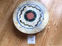 Top view showing drum side with red circle surrounded by blue and black patterns and snakes.