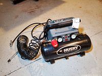 Front angle view of the black Husky air compressor with coiled air hose attached, showing the Husky logo and model details on the tank.
