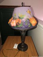 Full view of the lamp showing frosted glass shade with raised colorful flowers and decorative metal base