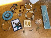 Photo of various bracelets, pendants, earrings, brooches, and a belt buckle laid out on a wooden surface.