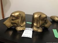 Pair of solid brass dog head bookends positioned side by side on a black surface.