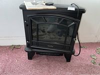 Black Duraflame electric heater with glass front and cord, placed indoors on carpeted floor.