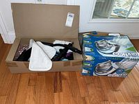 Cardboard box containing various fabric steamer accessories including brushes, steam heads, and microfiber cloths.