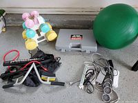 Overview of the lot showing dumbbells on rack, exercise ball, weight plate case, fitness bars, resistance band, and Wii gaming components