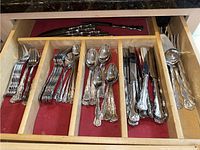 Drawer with multiple compartments holding forks, spoons, knives, and serving utensils with Reed & Barton ornate pattern