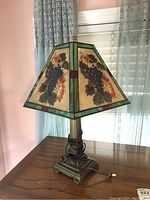 Photo showing full lamp with stained glass grape design on shade, bronze base, and electrical cord visible.