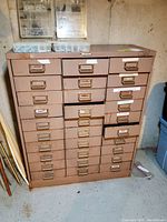 Front view of the vintage metal storage cabinet with 30 drawers, showing visible rust spots, scratches, and some drawer labels.