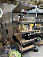 Full view of metal shelving unit showing five pressed wood shelves and gray metal frame in basement setting with various stored items on shelves.