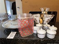 Wide view of serveware items on black surface showing glass jar, chip and dip bowl, crudit glass dishes and condiment holders