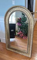 Full view of gold toned arched mirror with decorative textured frame and black bead-like accent details along inner edge.