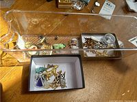 Collection of vintage pins and brooches in clear plastic box, showing variety of animal and military styles.