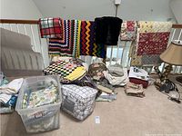 Full view of assorted quilts, afghans, sheets, blankets, and pillow cases with some items stored in plastic tubs, others folded and displayed on a carpeted floor and railing.