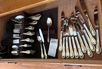 Full drawer view showing arranged flatware including forks, knives, spoons, and serving pieces with gold and silver decorative handles.