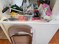 View of folding chair with plastic containers filled with various household items on a white surface.