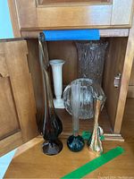 View of all six vases including the tall amber-colored art glass, white porcelain, clear Waterford crystal vases with star-cut and scalloped edges, clear round Waterford crystal vase, slender green base glass vase, and iridescent twisted vase.