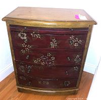Front view of vintage dresser showing four curved drawers with floral hand-painted design and round metal knobs.