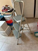 Side angle showing three textured anti-slip steps, beige metal frame, and rubber foot caps on tiled floor.