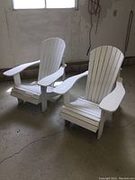 Two white painted wooden Adirondack chairs shown from front at an angle in a garage setting