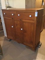 Front view of the antique wooden buffet showing two drawers on top and three cabinet doors below, all fitted with white round knobs.