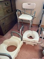 View showing two toilet seats with arm handles, a white shower chair, and a reach grabber tool on carpeted floor.