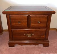Front view of one wooden bedside table showing the two small top drawers with round knobs and one large bottom drawer with brass handle.