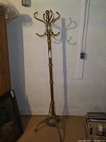 Full height view of vintage brass hall tree showing tall slim pole with multiple hooks at top and tripod base.