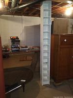 Full side view of tall, narrow white melamine CD tower against wall, showing its overall height and slim profile.