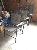 Three folding deck chairs with patterned taupe mesh and metal frames stored in a garage.