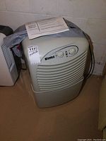 Full view of Kenmore dehumidifier on basement floor with owner's manual on top, visible power cord coiled at side.