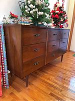 Front side view of nine drawer wooden dresser with mid century modern style and metal handles, showing overall condition and finish.