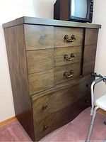 Full view of vintage wood dresser with five drawers, decorative brass handles, and a curved bottom drawer.
