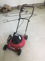 Full view of Spectrum electric lawn mower showing red deck, handlebar, wheels, and power cord.