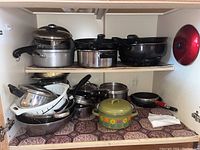 Photo of various pots and pans stored in a kitchen cabinet including saucepans, fry pans, strainer, and mixing bowl.