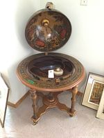Front view of globe bar cabinet opened showing interior compartments and exterior antique map design