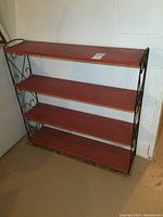Front view of vintage shelf showing four reddish-brown wooden shelves with black metal frame and scrollwork sides.