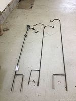 Three black metal shepherds hooks laid out on a concrete floor, showing full length and bottom prong design.