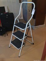 Full view of a white metal folding step ladder with three black non-slip steps and a rounded top handle.