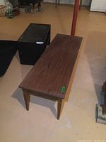 Vintage wood coffee table with wood grain finish and tapered legs shown from above at an angle in basement setting.