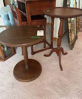 Photo showing two wooden pedestal tables, one with a round base and a straight central column, the other with a tripod base and turned legs.