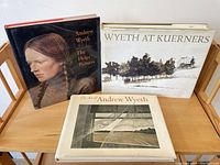 Photo of three Andrew Wyeth art books: The Helga Pictures, Wyeth at Kuerners, and The Art of Andrew Wyeth, all hardcover with dust jackets, placed on a wooden surface.