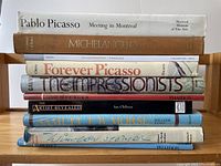 Photo of the spines of 10 art books arranged horizontally, showing titles and partial authorship on classic artists including Picasso, Michelangelo, Monet, and others.