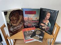 Five hardcover art books arranged on wooden shelf including Michelangelo The Painter, Italian Painting, Leonardo Da Vinci, Leonardo, and Mona Lisa The Enigma.