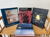 Four Latin American artist books arranged on a wooden table: Antonio López, Tamayo, Marcello Suarez Nakar, and Dreams are Colder than Death.