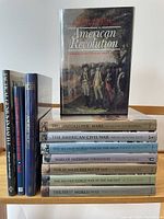 Photo of all 11 military history books, standing and stacked, showing front covers and spines with titles.